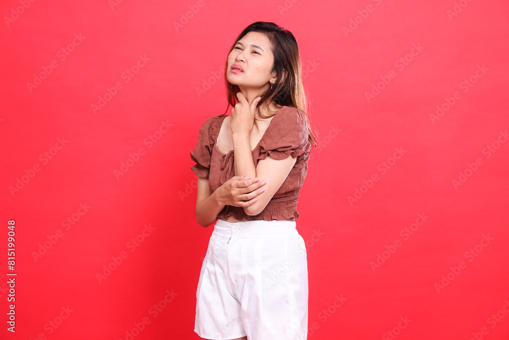 Expression of an indonesia woman who is sick with a candid throat pain wearing a brown blouse top and shorts on a red background. for health, lifestyle and advertising concepts Expression of an indonesia woman who is sick with a candid throat pain wearing a brown blouse top and shorts on a red background. for health, lifestyle and advertising concepts