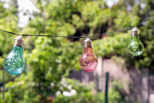 Colorful light bulbs hanging on a chain outdoors, garden decoration, fairy lights