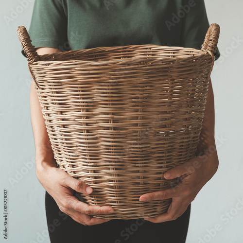 A cropped image of a beautiful young woman holding a wicker laundry basket of clothes with a white background.