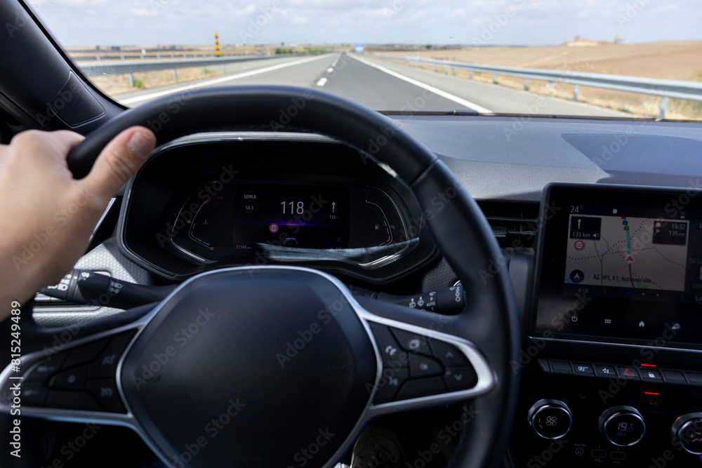 Driver view to the speedometer at 118 kmh, on a road blurred. Daylight view from inside a car of driver POV of the road landscape. Driver view to the speedometer at 118 kmh, on a road blurred. Daylight view from inside a car of driver POV of the road landscape.