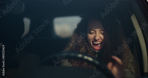 An emotional teenage girl with curly hair and braces screams while gripping the steering wheel of a car, expressing stress or fear. photo