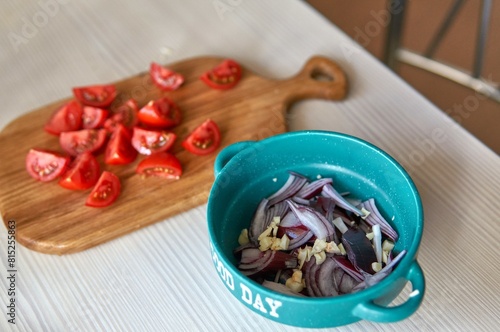 Lettuce in the process of cooking, red onion and garlic are in a bowl, tomatoes on a wooden board in the background, cut into pieces