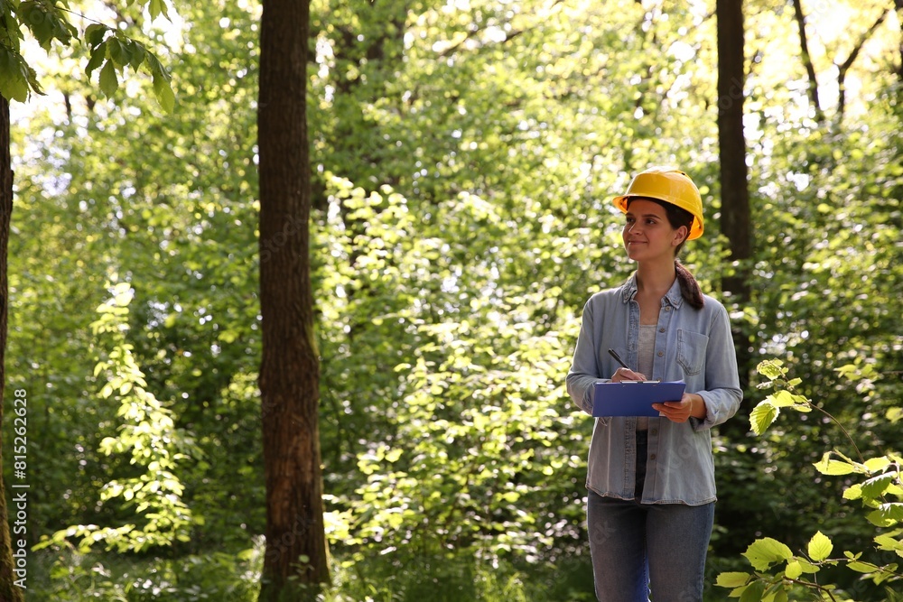 Forester with clipboard examining plants in forest Forester with clipboard examining plants in forest