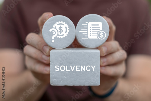 Business man holding white blocks with icons sees word: SOLVENCY. Solvency business finance concept. Creditworthiness, banking conditions, credit funds.