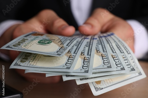 Money exchange. Man counting dollar banknotes at wooden table, closeup