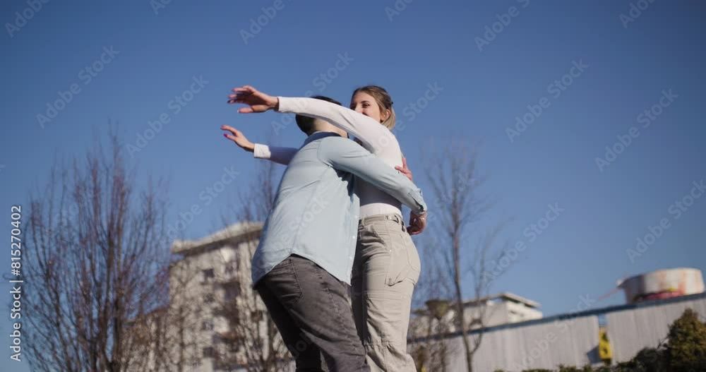 An affectionate moment between a man and a woman, sharing a playful hug and spinning around in a sunny, outdoor urban landscape. An affectionate moment between a man and a woman, sharing a playful hug and spinning around in a sunny, outdoor urban landscape.