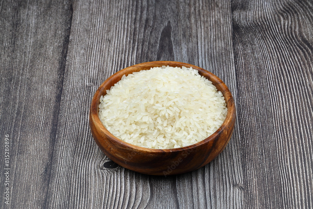 Raw white rice on black background. Long uncooked rice in wooden plate. Natural organic food. Traditional Asian cereal culture. Raw white rice on black background. Long uncooked rice in wooden plate. Natural organic food. Traditional Asian cereal culture.