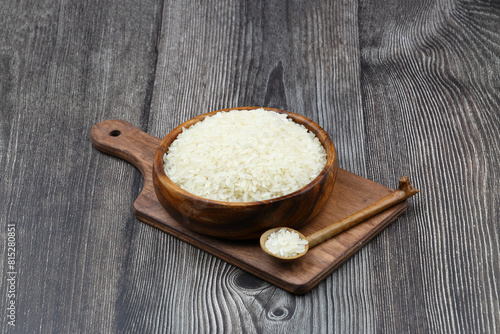 Raw white rice on black background. Long uncooked rice in wooden plate. Natural organic food. Traditional Asian cereal culture.