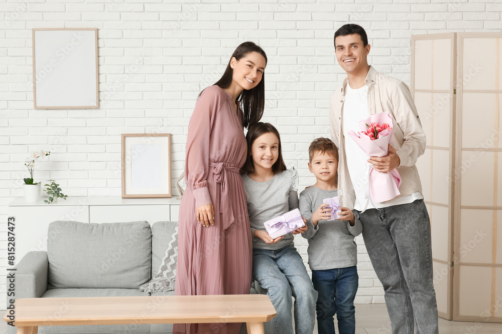 Happy family greeting their mother with Mothers Day with flowers and gift in living room Happy family greeting their mother with Mothers Day with flowers and gift in living room