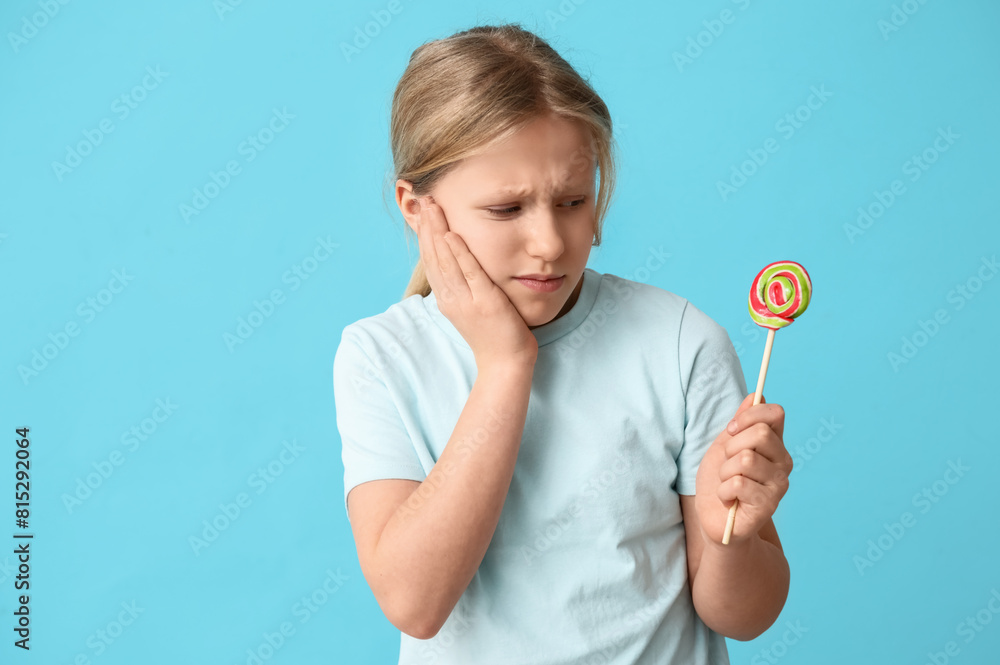Young girl holding lollipop and suffering from toothache on blue background Young girl holding lollipop and suffering from toothache on blue background