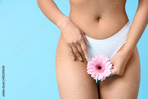 Beautiful young woman in panties with gerbera flower on blue background, closeup