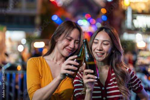 Asian woman friends hold bottle of beer, having party infront of bar. 