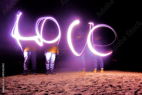 Night photo in motion with soft blur and long exposure. Married couple wrote word Love in purple light. Concept of positive emotion, February 14, Valentine's day, marriage, wedding, family, holiday