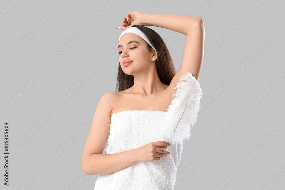 Young woman in towel with clean armpits and feather on light background Young woman in towel with clean armpits and feather on light background