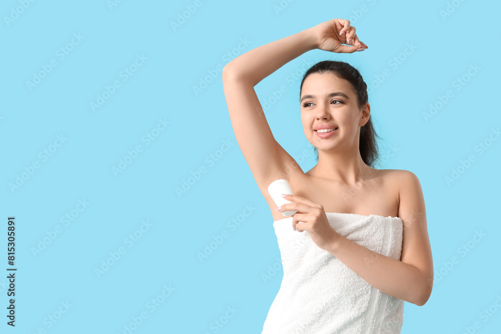 Young woman in towel applying deodorant on blue background Young woman in towel applying deodorant on blue background