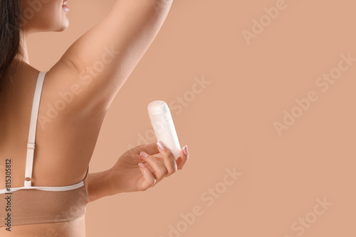 Young woman applying deodorant on brown background, back view