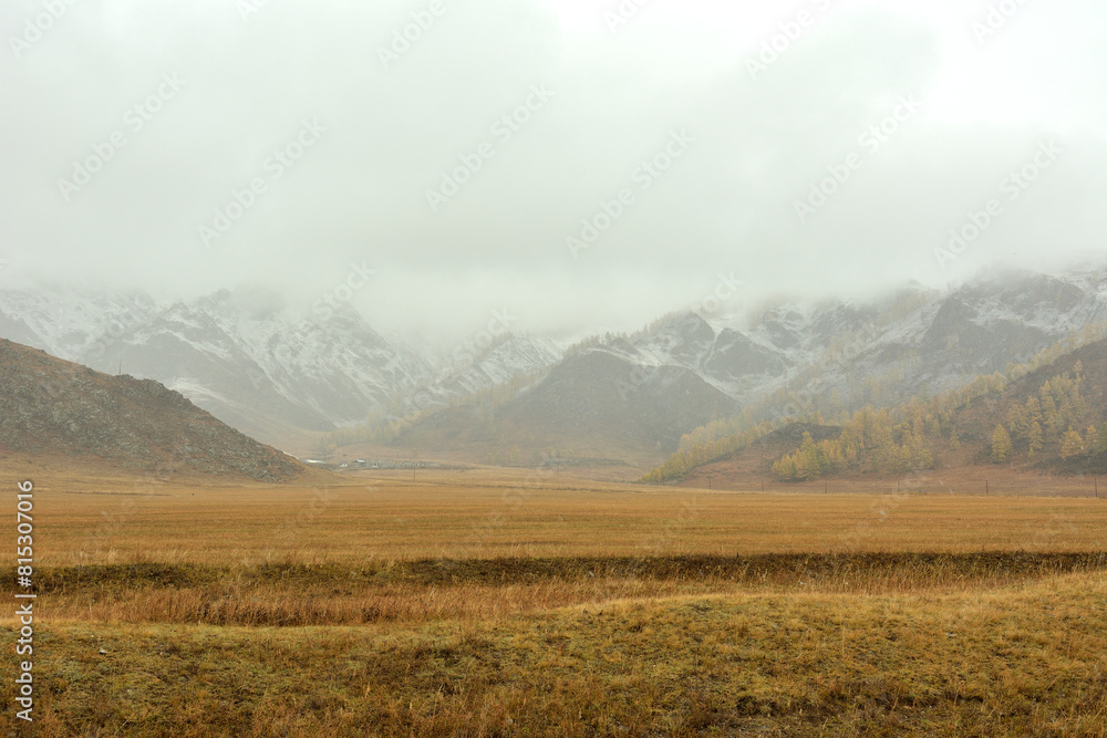 Flat steppe with yellowed grass at the foot of high mountain ranges with peaks in thunderclouds.