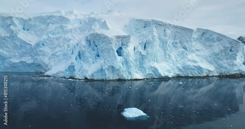 Beautiful towering huge iceberg floating tranquil cold Antarctica ocean. Snow covered blue ice wall glacier reflecting calm water. Ecology, melting ice, climate change and global warming concept