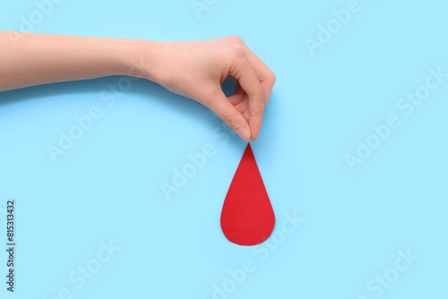 Female hand with paper blood drop on blue background. World Blood Donor Day photo