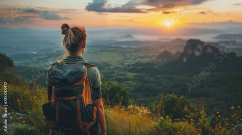 Back view of a woman with a backpack overlooking a stunning sunset from the top of a mountain.