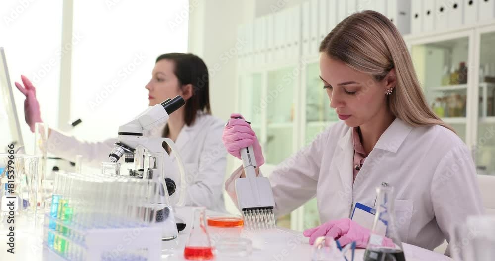 Two scientists in a laboratory perform an experiment using a multichannel pipette Two scientists in a laboratory perform an experiment using a multichannel pipette