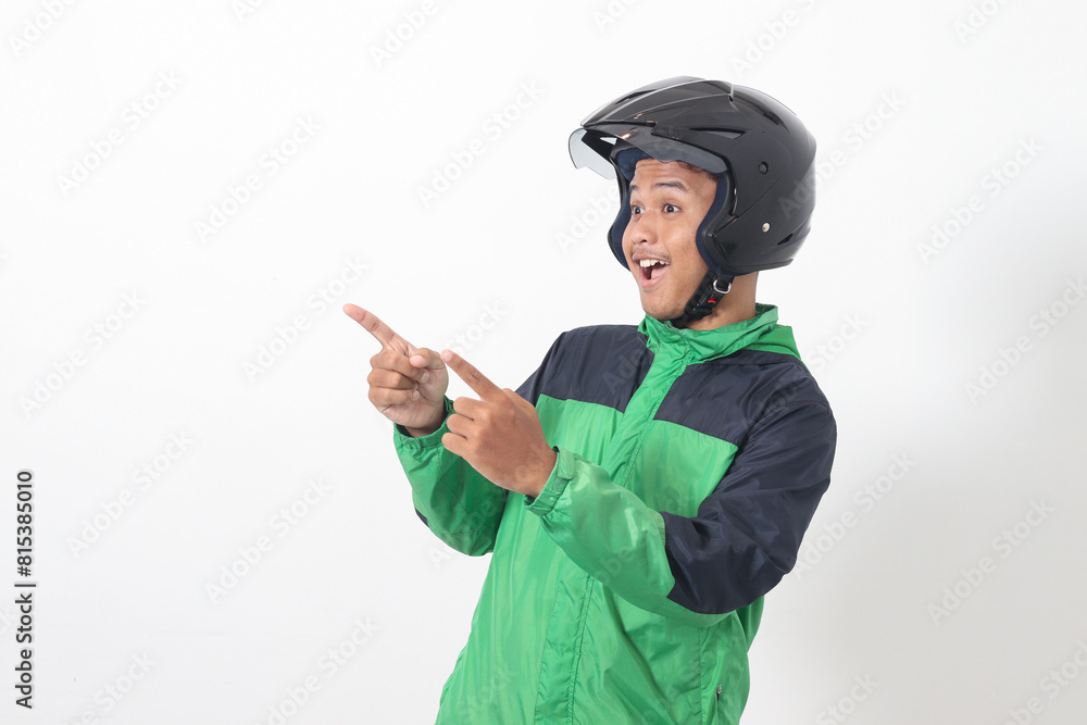 Portrait of Asian online taxi driver wearing green jacket and helmet pointing at empty space with finger. Isolated image on white background Portrait of Asian online taxi driver wearing green jacket and helmet pointing at empty space with finger. Isolated image on white background