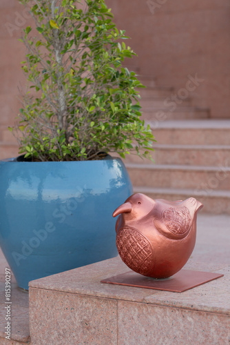 An elegant copper bird sculpture and a lush plant adorn stone steps, creating a serene atmosphere.