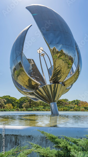An unusual sculpture in the form of a huge metal flower is installed in the city park in a pond. Shiny curved petals, long stamens against the blue sky.  Green vegetation. Buenos Aires. Argentina. photo