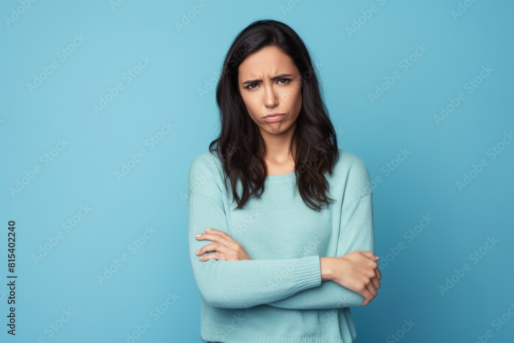 Upset young woman with crossed arms, frowning, light turquoise background Upset young woman with crossed arms, frowning, light turquoise background