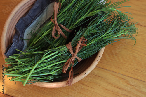 Bunch of fresh Salsola soda in a basket on wooden table. Italian Barba di frate or Agretti or Saltwort on wooden background photo