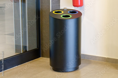 Metal trash can for disposing of plastic, paper and waste placed next to a wall in the hallway of a modern building	