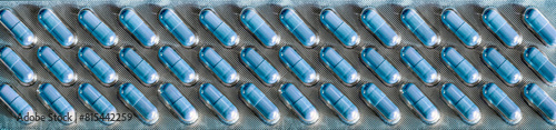 Light blue pills are packed in rows in a long transparent blister that takes up the entire background. Medical background for industry, business, pharmacies, clinics.