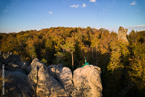 Woman practicing yoga and meditation on the top of huge boulder in the evening. Beautiful sunset, autumn forests, rocks and hills on background. Aerial drone view