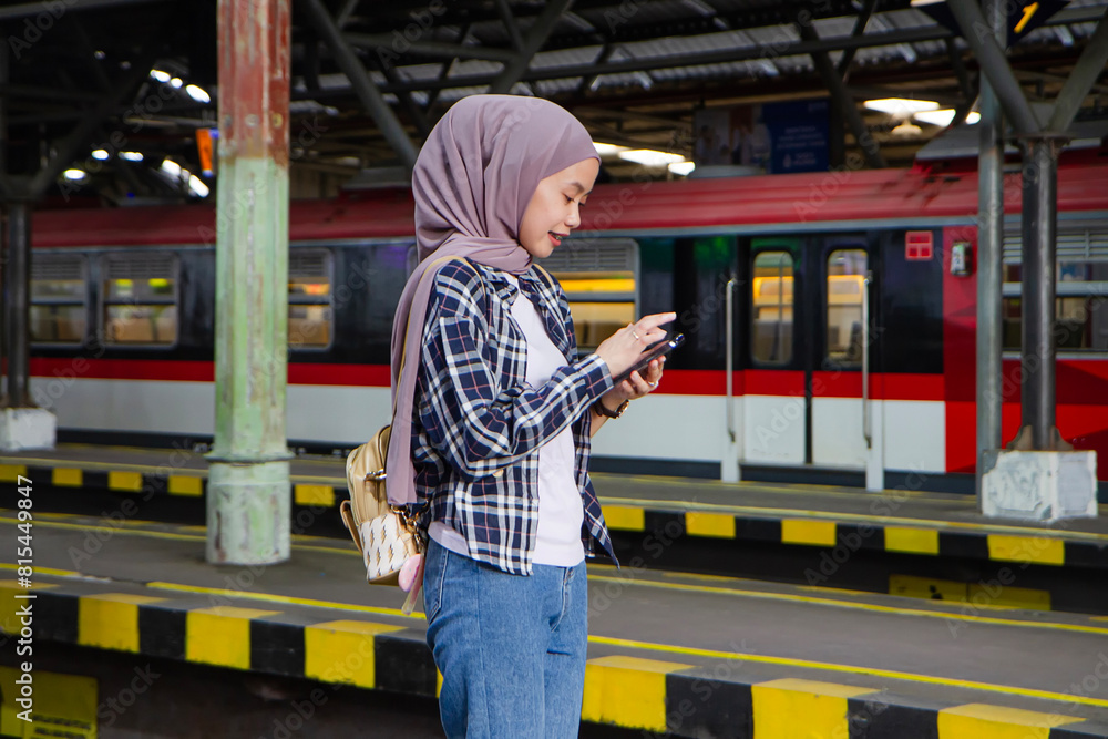happy asian muslim woman holding mobile phone while standing on train station platform. traveling concept happy asian muslim woman holding mobile phone while standing on train station platform. traveling concept