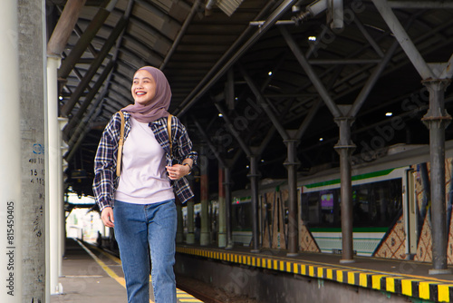 happy asian muslim woman wearing casual outfit walking on train station platform. traveling concept