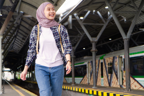 happy asian muslim woman wearing casual outfit walking on train station platform. traveling concept