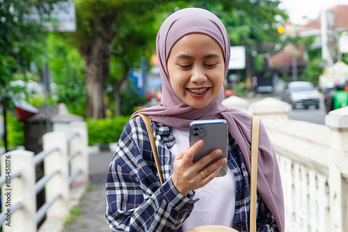 happy asian muslim woman walking on the street while looking at her mobile phone