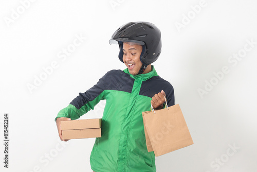 Portrait of Asian online courier driver wearing green jacket and helmet giving craft paper shopping bag and box package. Isolated image on white background photo