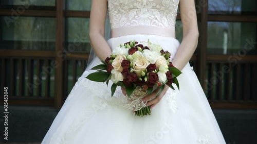 The bride holds the wedding bouquet in her hands in front of her. The veil flies in the wind.