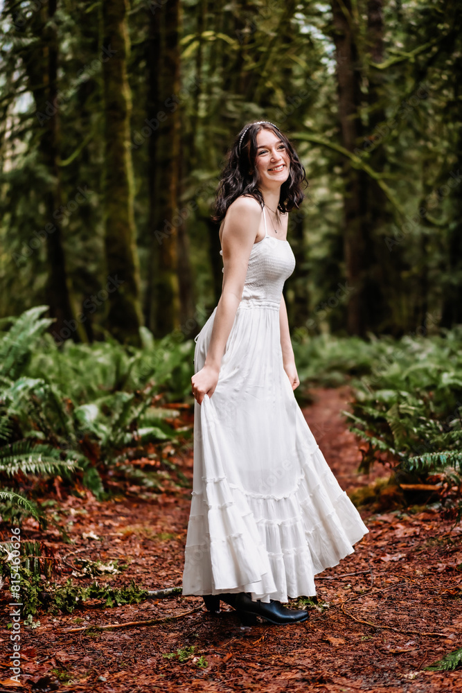 Teen girl holding her white flowy dress while smiling in the woods Teen girl holding her white flowy dress while smiling in the woods