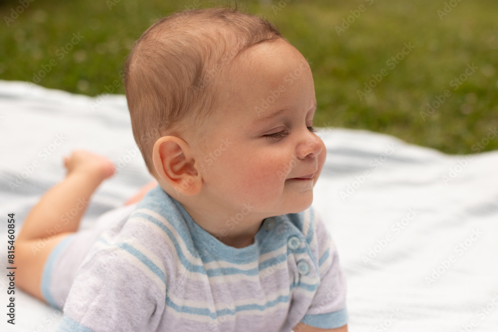 Smiling baby boy lying on a blanket outdoors, enjoying a sunny day Smiling baby boy lying on a blanket outdoors, enjoying a sunny day