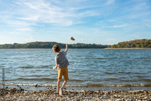 young boy throws rock into lake with waves on a sunny day