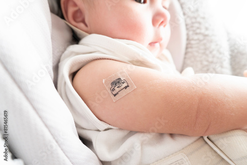 Fotografie Band-aid with character on it on baby's right arm with red skin after vaccinatio
