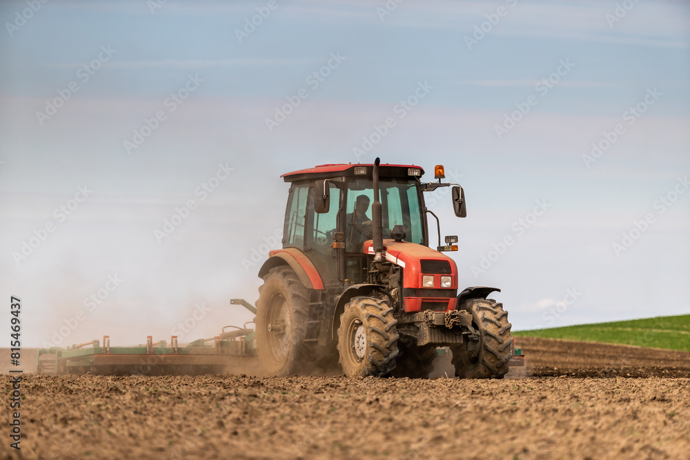 Farmer works the land, plowing a field with a modern red tractor on a sunny day Farmer works the land, plowing a field with a modern red tractor on a sunny day