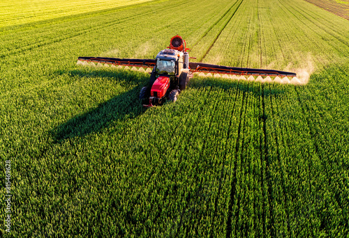 Drone shot of a farmer in red tractor spraying pesticides wheat in a lush green farmland photo