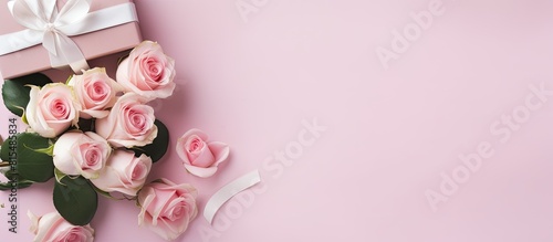 A top down view of a cluster of pink roses a white gift box a notebook and a vintage ribbon on a pink backdrop This setup is perfect for mother s day Valentine s day or a wedding event There s ample