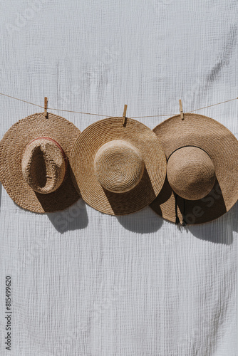 Three straw hats hanging on a rope over white cloth with sunlight shadows