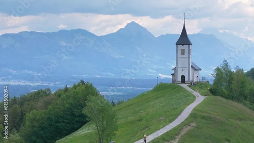 Flying by the Catholic church at the top of the hill, the St. Primus and St. Felician church at Jamnik, Slovenia, Kamnik Savinja Alps in background. Drone shot, 4K, 60FPS photo