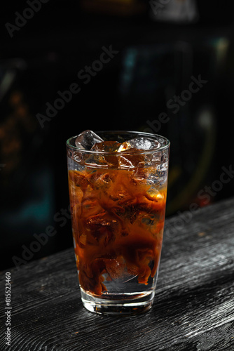 A glass of refreshing espresso tonic cold coffee drink with ice cubes, on wooden table