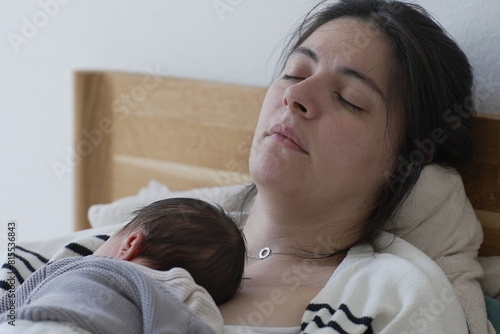 A serene moment of a mother sleeping with her newborn baby resting on her chest. The baby, dressed in a cozy gray sweater, and the mother both exhibit a peaceful and loving bond,